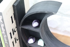 Detail of black moon-shaped wooden shelf with polished crystals in a cozy home setting