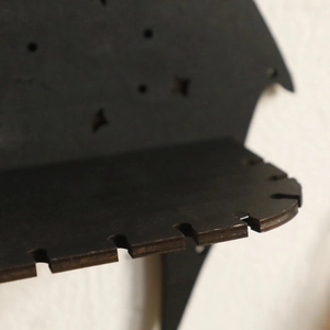 Detail of laser-cut wooden dragon shelf showing precise grooves and dark finish texture