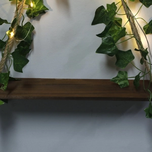 Close-up of wooden swing shelf with hemp rope, faux ivy leaves and warm LED fairy lights