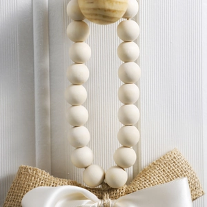 Detail of wooden bead garland with burlap and satin bow on a white textured background