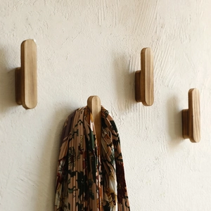 Detail showing natural wood grain wall hooks with floral scarf hanging on beige wall