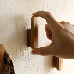 Hand holding a creative solid wood wall hook with natural grain on a white textured wall
