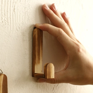 Close-up of L-shaped walnut wood wall hook with natural grain on textured surface
