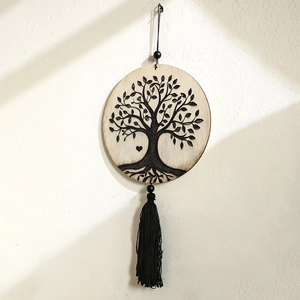 Detail view of wooden Tree of Life wall hanging with black tassels on a textured surface