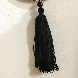 Detailed view of modern black cotton tassels with dark wooden bead on wall