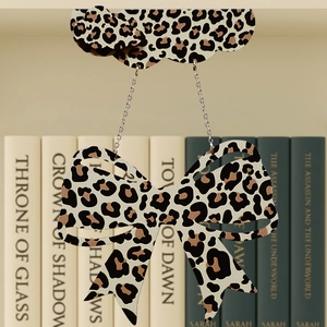 Close-up of a wooden leopard print bow pendant with metallic chains against books
