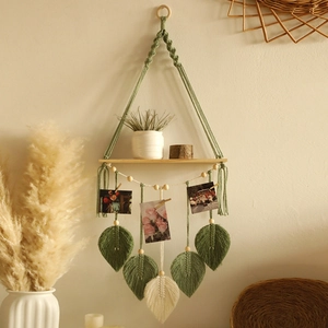 Detail of bohemian woven wall shelf with wooden plate, clips for photos and leaf tassels