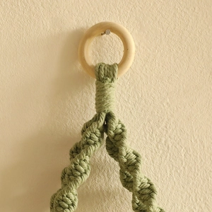 Detail of hand-woven green macrame leaf pattern and natural wooden hanging ring