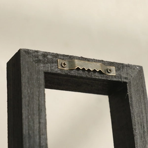 Close-up of sawtooth metal hanger and screws on the back of black wooden wall frame
