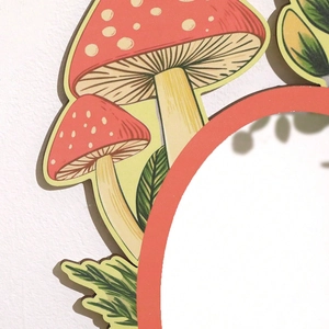 Detail of red mushroom and green leaf wooden pendant showing fine craftsmanship and texture