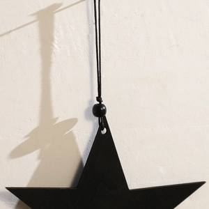 Close-up of black wooden star wall hanging with minimalist tassel and hanging rope detail