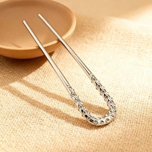 Épingle à cheveux argentée en forme de U avec strass sur un fond texturé beige élégant