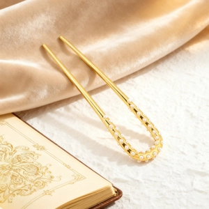 Détail d'une épingle à cheveux dorée en U avec perles sur fond de velours champagne