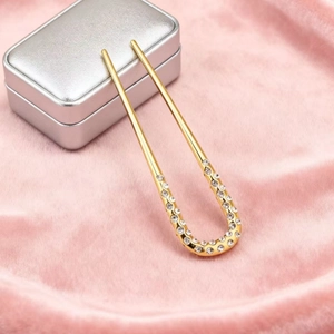 Vue détaillée d'une épingle à cheveux dorée en U avec strass sur peluche rose douce