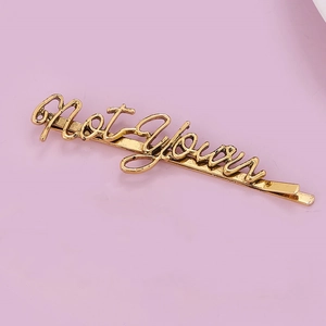 Macro view of retro golden metal hair clip featuring Not Your letter engraving