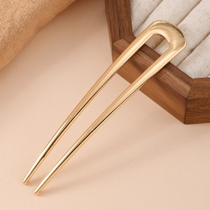 Close-up of a polished golden U-shaped hair pin for minimalist styling on a wooden tray
