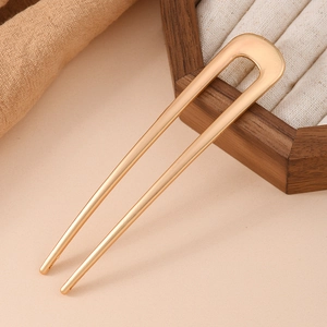 Detailed view of a golden U-shaped hair pin with matte finish on a minimalist background