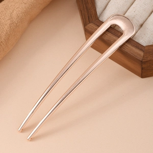 Detailed view of a polished U-shaped rose gold metal hair pin on a wooden jewelry box