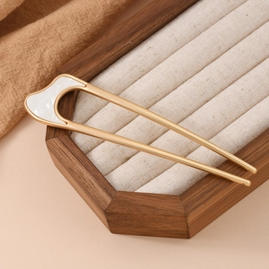 Detailed close-up of a matte gold U-shaped hairpin with white enamel on a wood stand