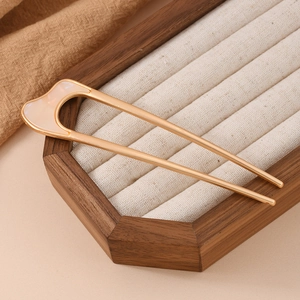 Close-up of golden U-shaped hair pin with pink mother-of-pearl inlay on wooden tray