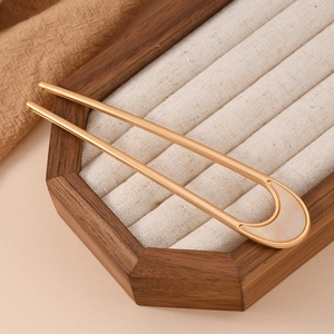 Detail view of U-shaped gold alloy hairpin with shell inlay on a wooden jewelry display