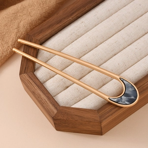 Detail of a minimalist gold U-shaped hair pin with marble texture on a display tray