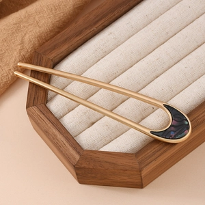 Detailed close-up of a U-shaped gold hairpin with dark inlay on a velvet jewelry tray