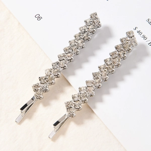 Elegant pair of silver-tone hair clips with rows of sparkling rhinestones on fabric background