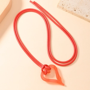 Close-up of red resin heart pendant on woven rope cord over minimalist textured background