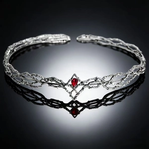 Macro shot of silver branch crown with a red teardrop gemstone on reflective surface