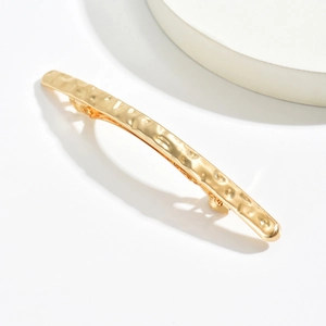 Barrette à cheveux dorée en métal avec texture martelée sur fond blanc minimaliste