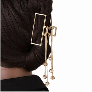 Détail de la pince à cheveux dorée avec longs glands et perles brunes sur chignon bas
