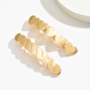 Golden heart and twisted metal hair clips set against a minimalist white background