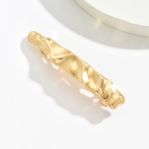 Detail showing high-shine gold-tone metal hair claw clip with irregular wave pattern texture
