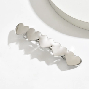 Polished silver metal hair clip with five linked hearts on a minimalist white display
