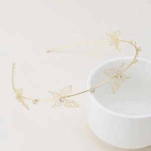 Elegant gold double-layered headband with hollow rhinestone butterfly accents on a ceramic cup
