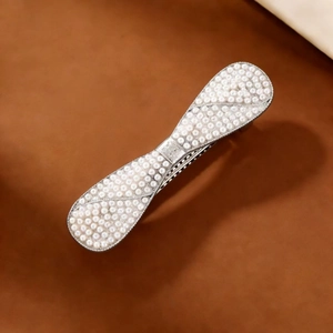 Detailed shot of bow-shaped hair clip with white pearls on brown leather background