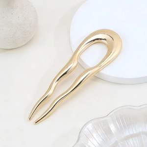 Minimalist U-shaped wavy hair fork in polished gold finish on a luxury display stand