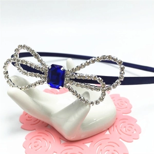 Navy blue rhinestone bow headband with emerald cut crystal center on ceramic display