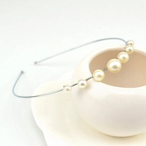 Primer plano de una elegante diadema plateada con perlas sobre un jarrón blanco
