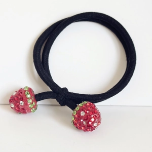 Gros plan détaillé d'un élastique à cheveux noir avec deux breloques fraises en strass rouges
