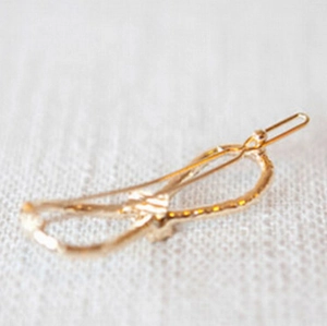 Detailed close-up of golden metal bow hair clip with textured surface on fabric background
