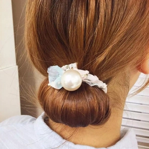 Détail d'un chouchou perle élégant avec tissu floral bleu sur un chignon brun