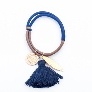 Détail de l'élastique à cheveux avec pompon bleu, pendentif feuille et médaille gravée