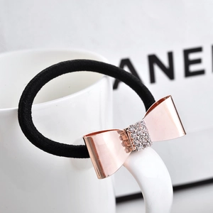 Détail d'un chouchou avec nœud en or rose orné de strass sur un élastique noir robuste