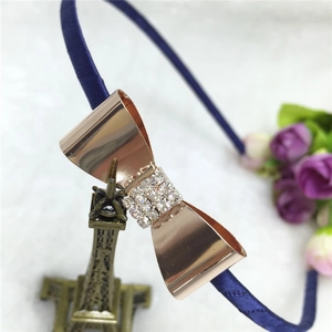 Détail d'un serre-tête bleu marine avec nœud en strass or rose sur fond en peluche blanche