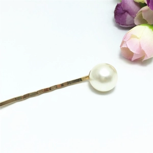 Detailopname van een gouden haarspeld met een grote crèmekleurige parel op witte basis