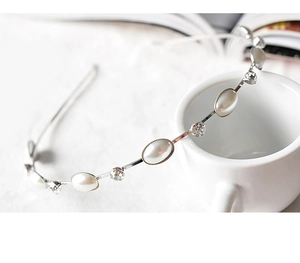 Detail eines schmalen Haarreifs mit Perlen und Strasssteinen auf weißer Tasse