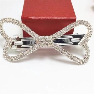 Détail d'une pince à cheveux en forme de nœud argenté ornée de strass brillants sur blanc