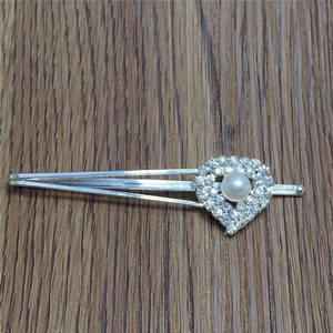 Détail d'une barrette argentée avec strass et perle en forme de cœur sur bois sombre